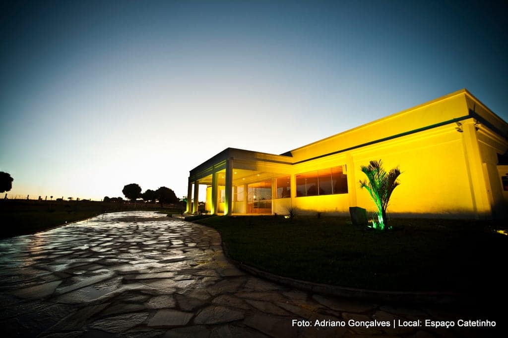 Fachada iluminada do salão ao entardecer, vista do caminho de pedra