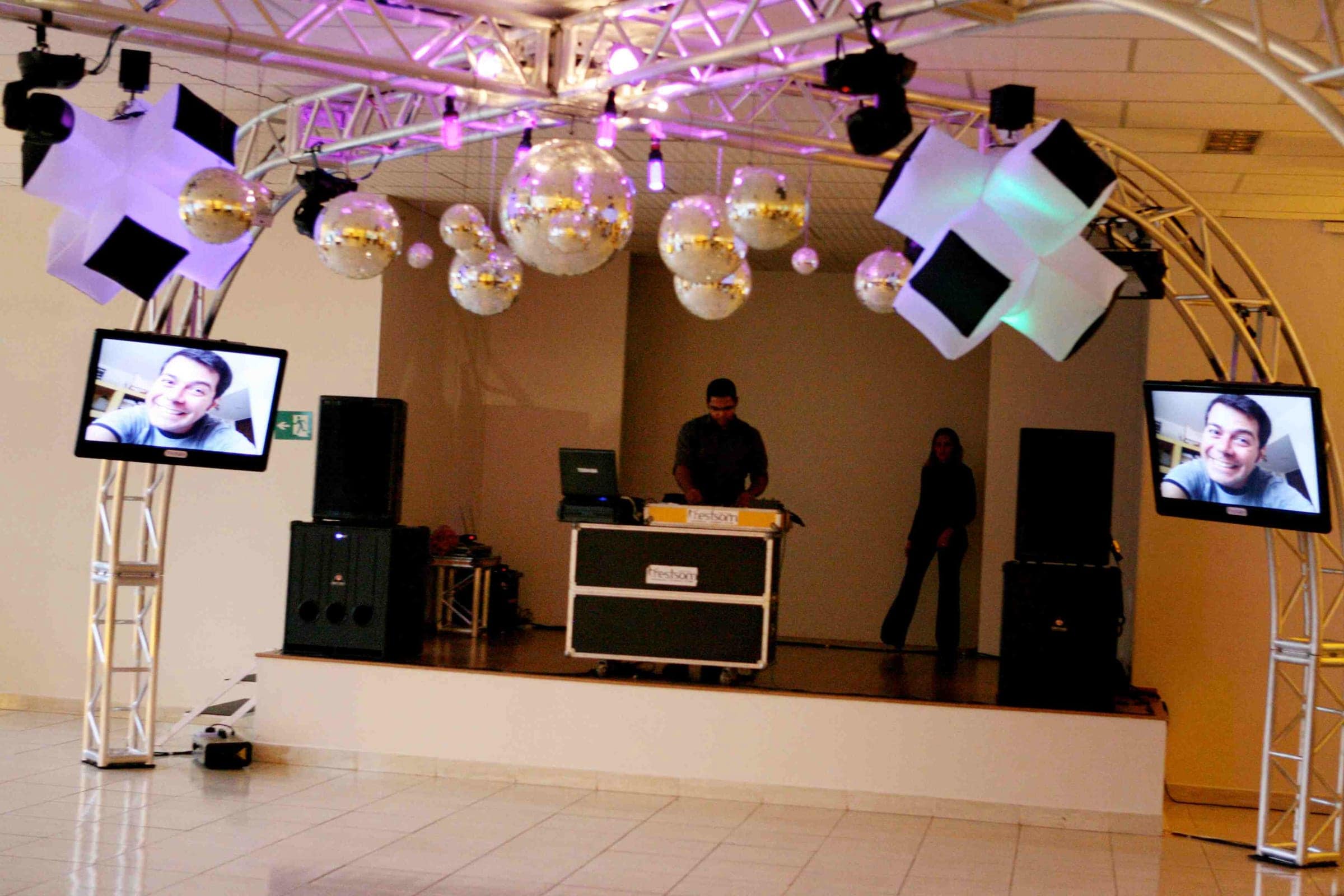 Salão preparado para festa, com globos de espelho, telões e estrutura de som e DJ