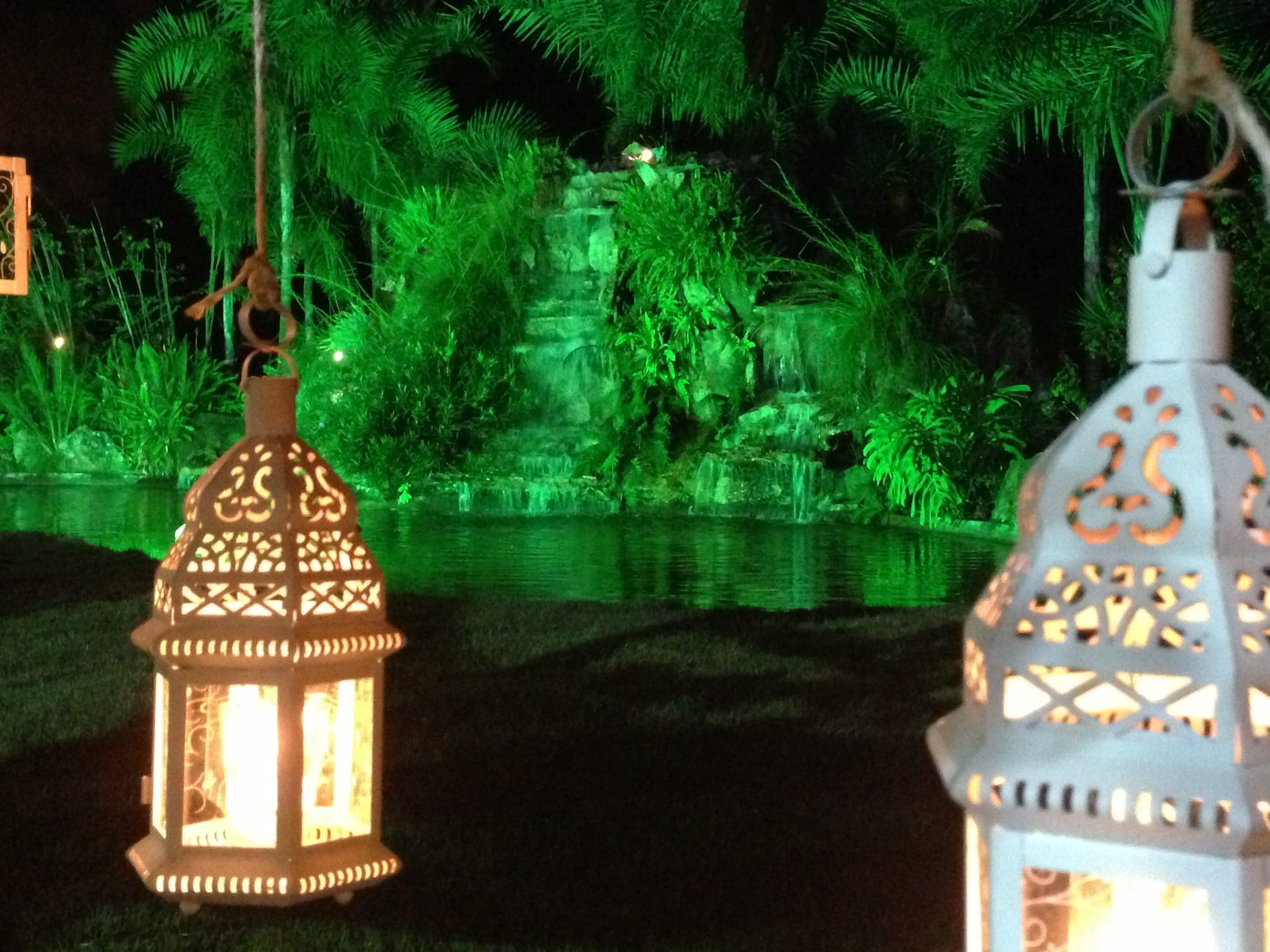 Lanternas marroquinas acesas no jardim à noite, com a vegetação iluminada em verde