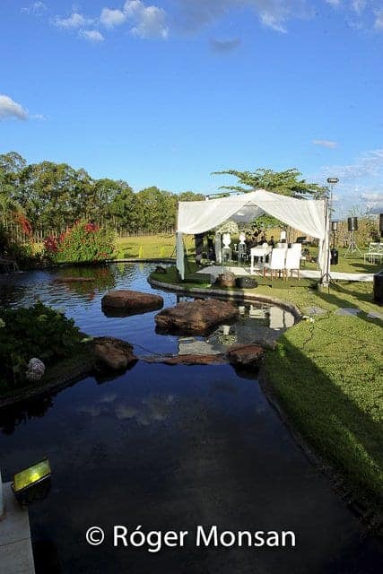 Riacho com pedras no paisagismo, com tenda branca montada ao fundo