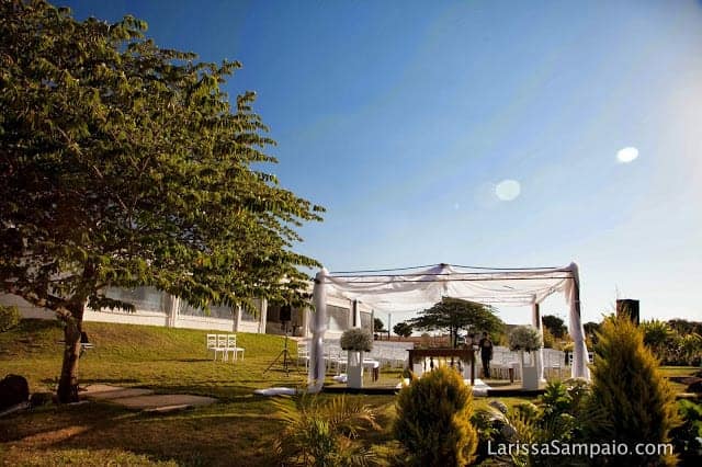 Área externa gramada com tenda branca montada entre as árvores