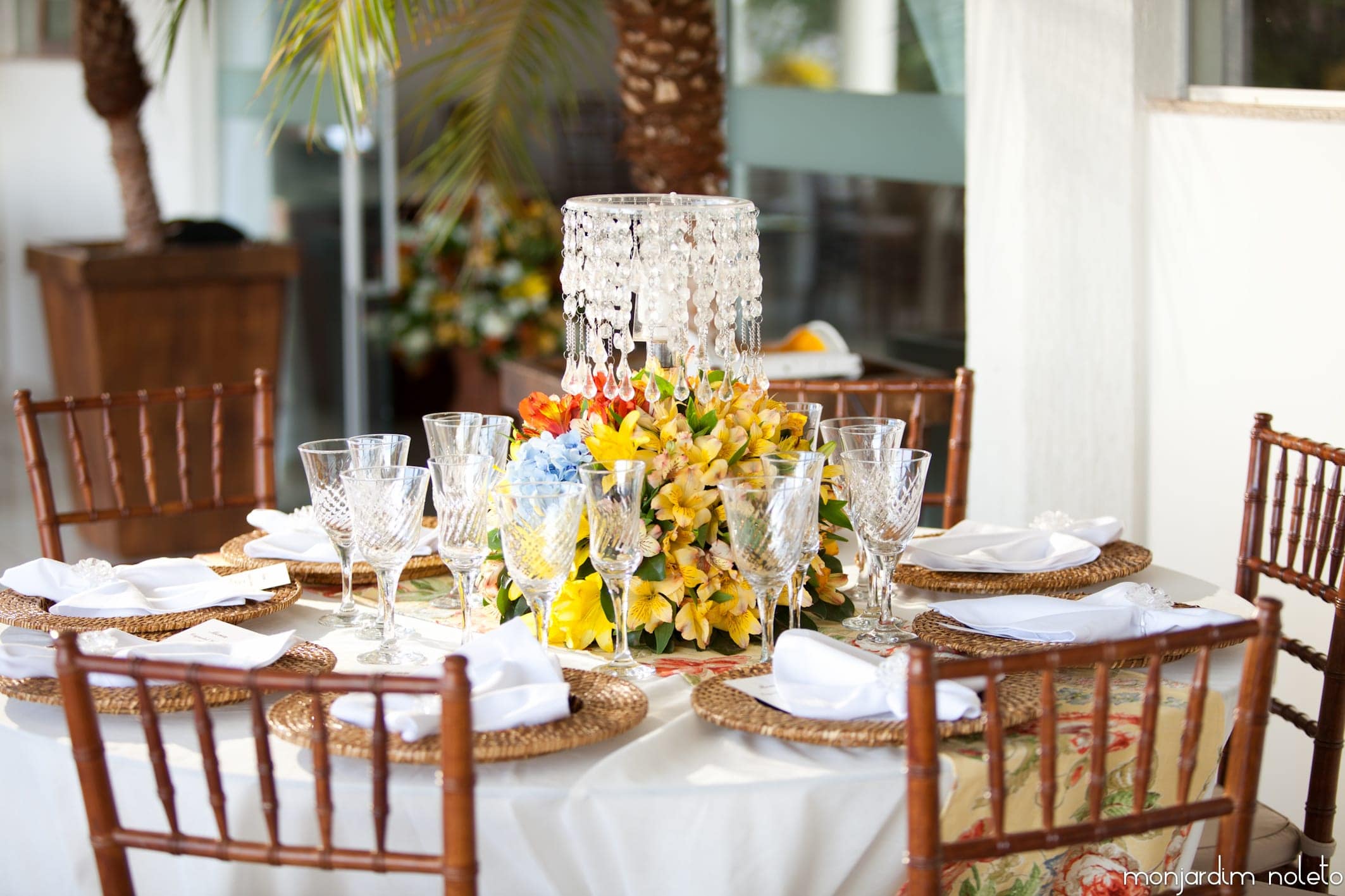 Mesa posta com cristais, flores amarelas e cadeiras Tiffany