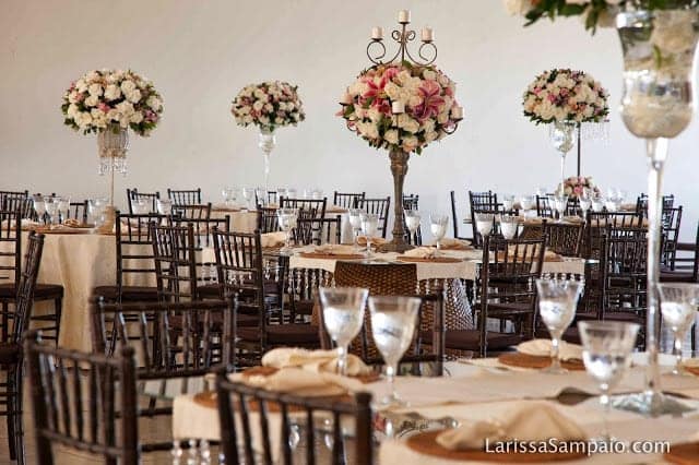 Salão com mesas redondas e arranjos florais altos ao centro