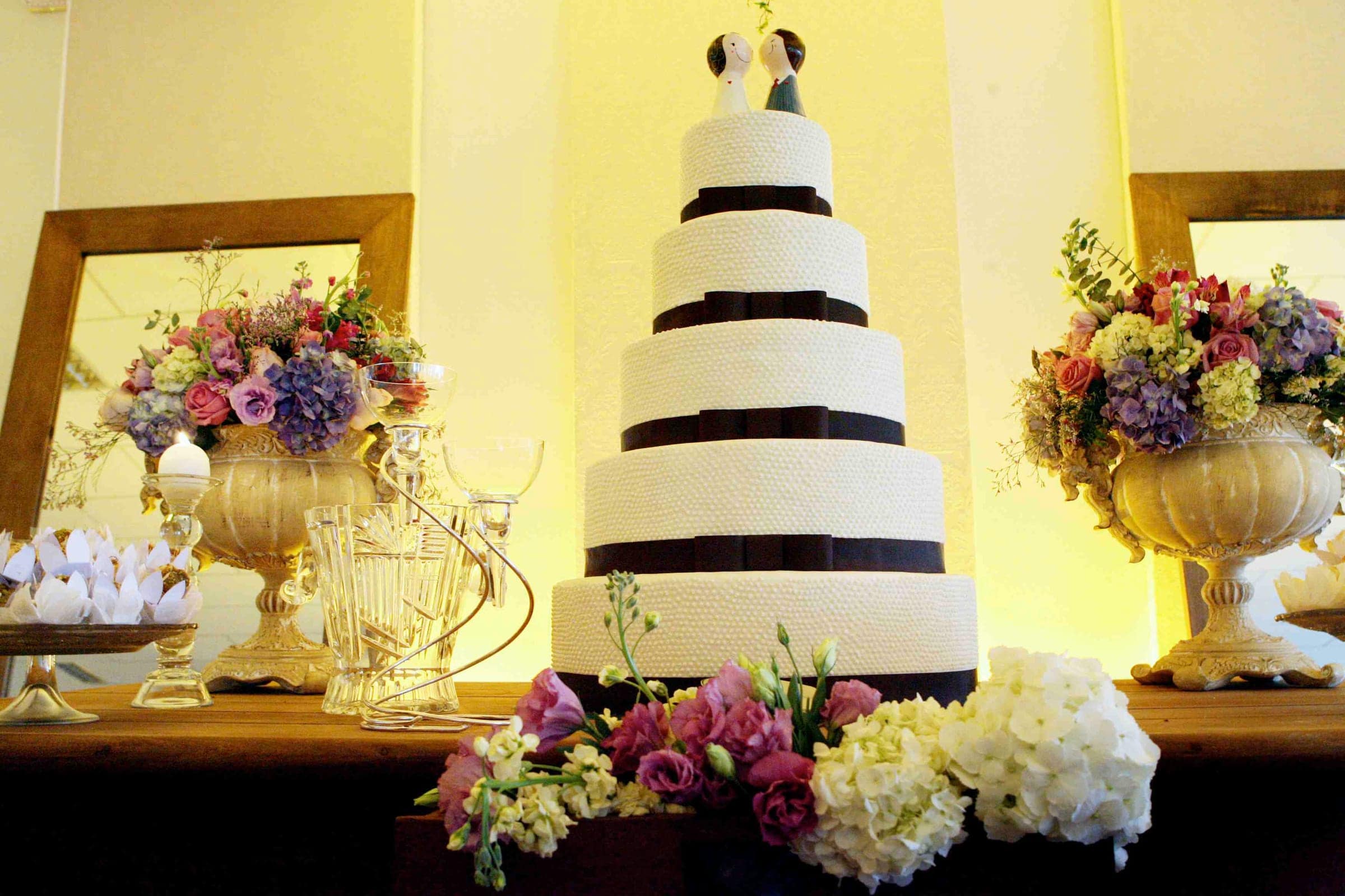 Bolo de casamento listrado em preto e branco entre arranjos florais, no salão