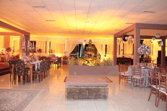 Salão iluminado em luz dourada, com mesas postas e pista ao centro