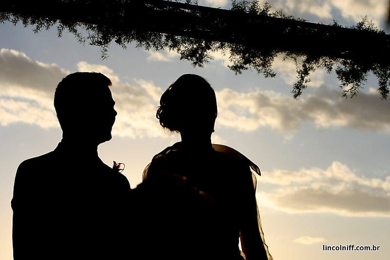 Silhueta do casal contra o pôr do sol, sob a copa de uma árvore
