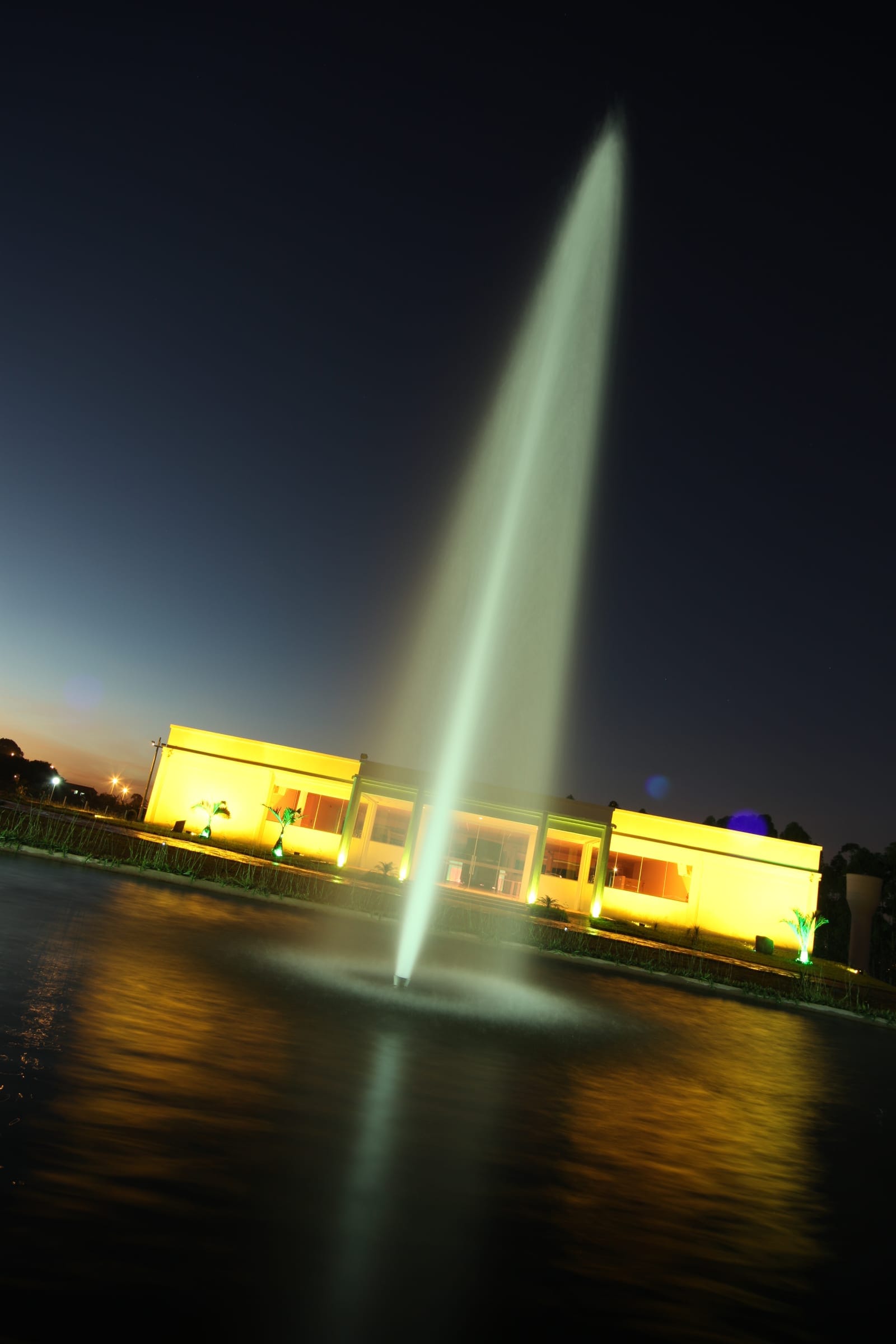 Fachada do salão iluminada à noite, refletida no espelho de água