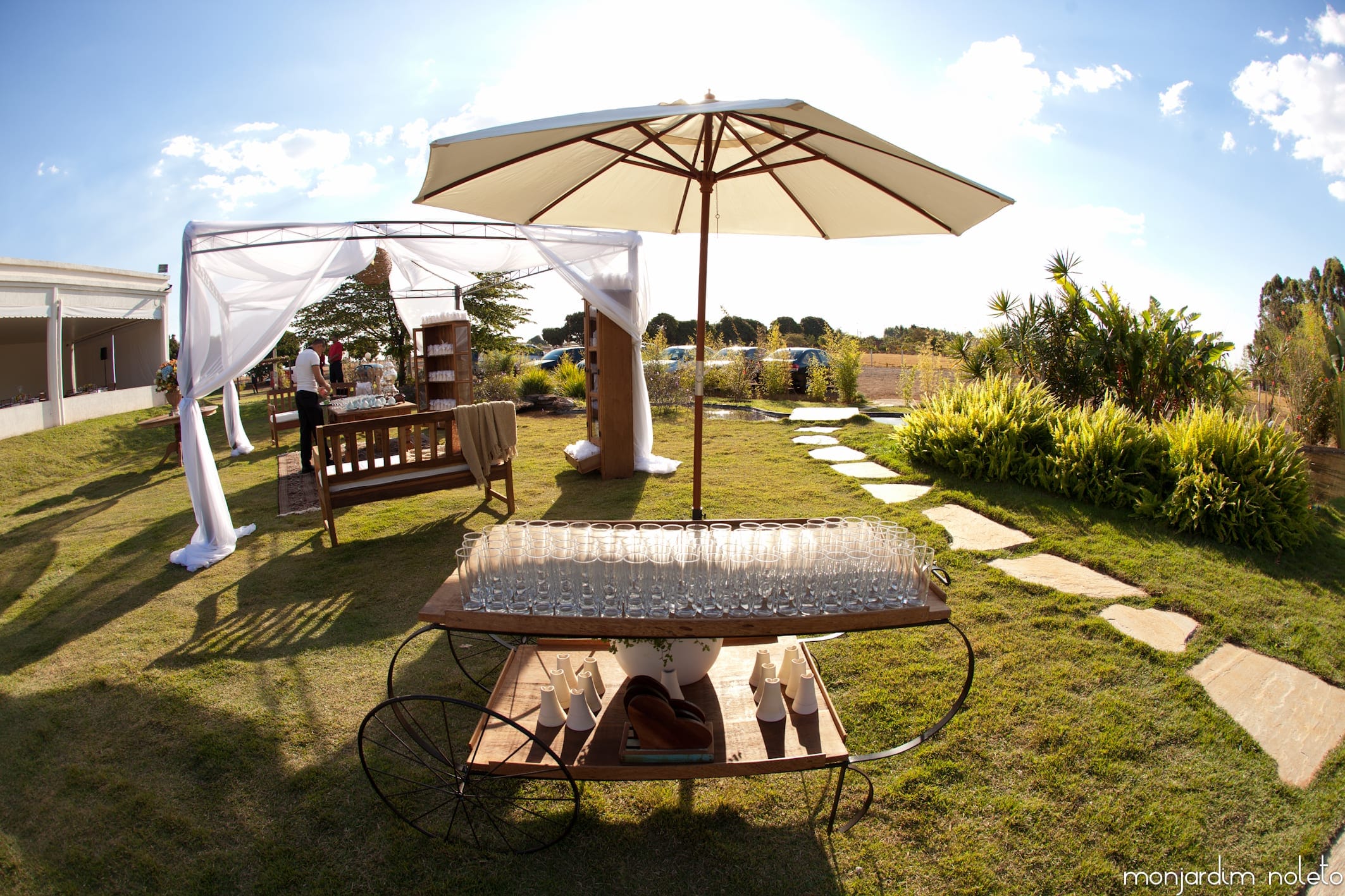 Lounge externo com guarda-sol, banco e mesa de apoio sobre o gramado, durante o dia
